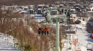 three people riding ski lift near village during day